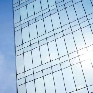 Close-up view of a modern glass building reflecting the blue sky and sunlight, featuring stainless steel window frames.