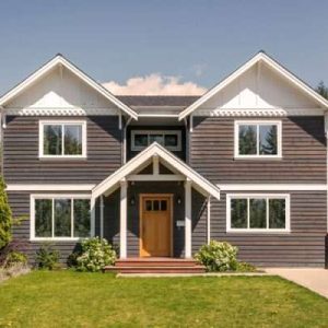 A modern two-story house with dark exterior siding and large reflective windows, showcasing the benefits of TrueVue window film.
